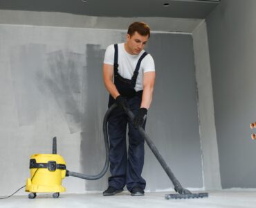 male worker in overall vacuum cleaning during apartment renovation.