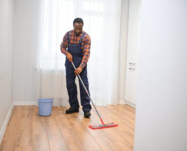 Young african man washes the floor with a mop in the room.