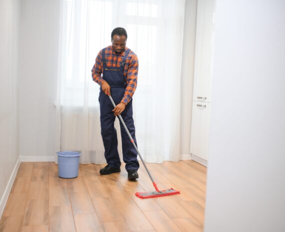 Young african man washes the floor with a mop in the room.